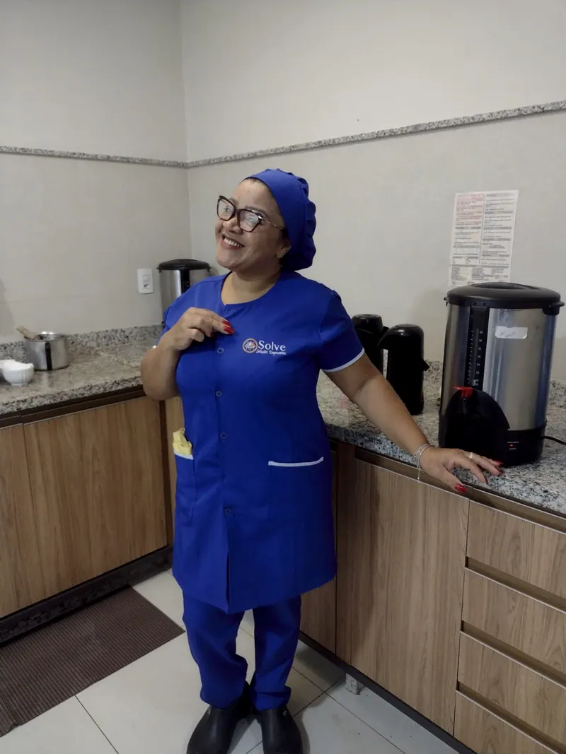 Funcionária da Solve, de uniforme azul, sorrindo numa copa ao lado das garrafas de café
